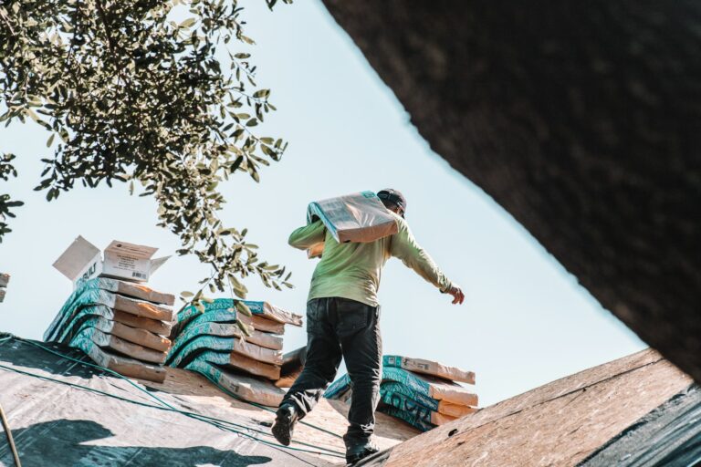 Roofer carrying a bundle of shingles across a residential roof