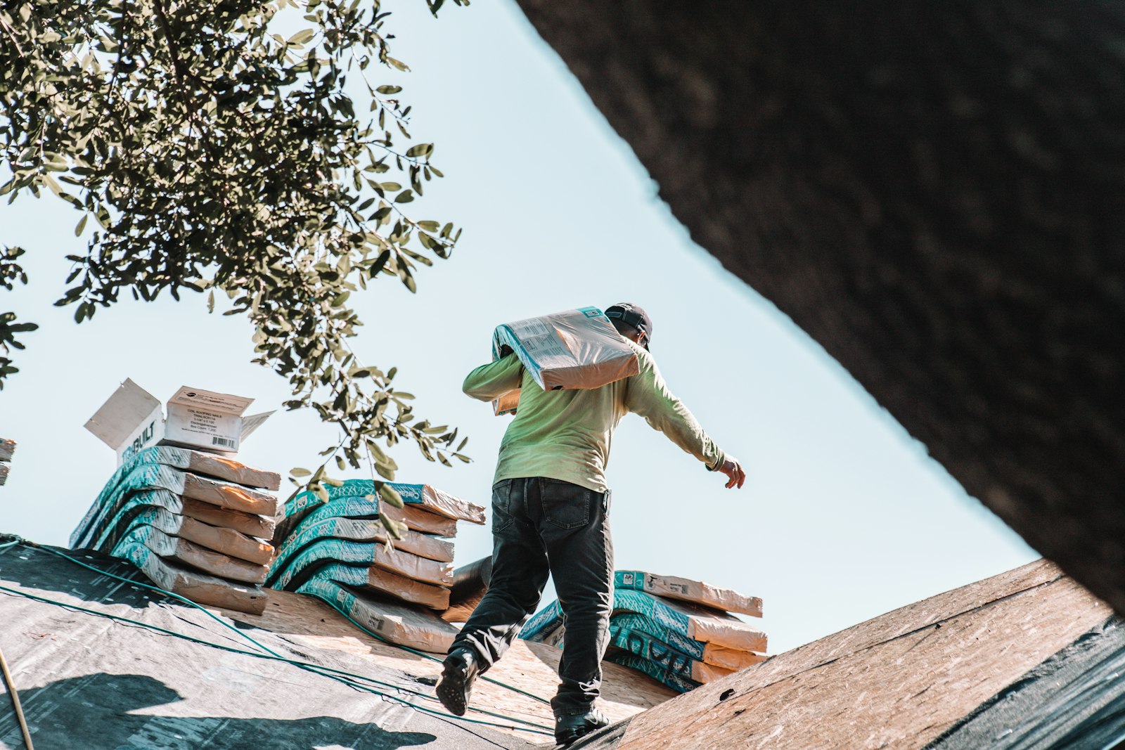 Roofer carrying a bundle of shingles across a residential roof